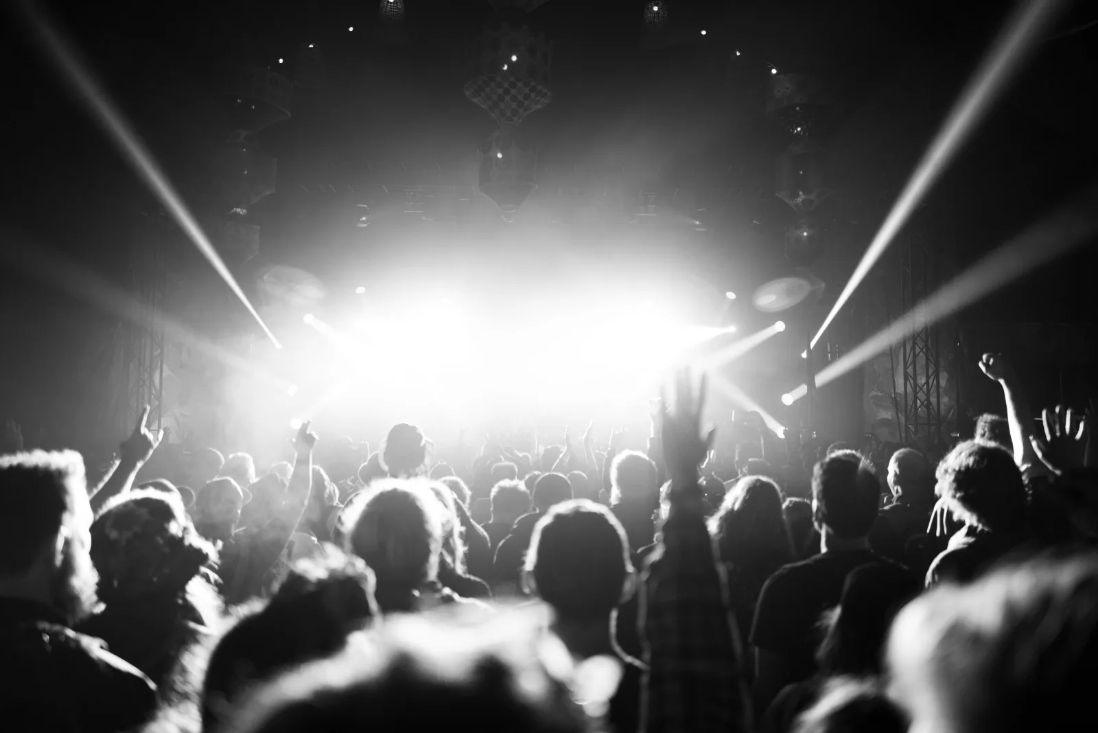 A crowd seen from behind, facing a brightly lit stage with beams of light overhead.